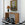 Wicker console table with lamp, flowers, and framed artwork on a checkered floor.