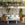 Outdoor patio with wicker furniture, table, and plants against a white picket fence.